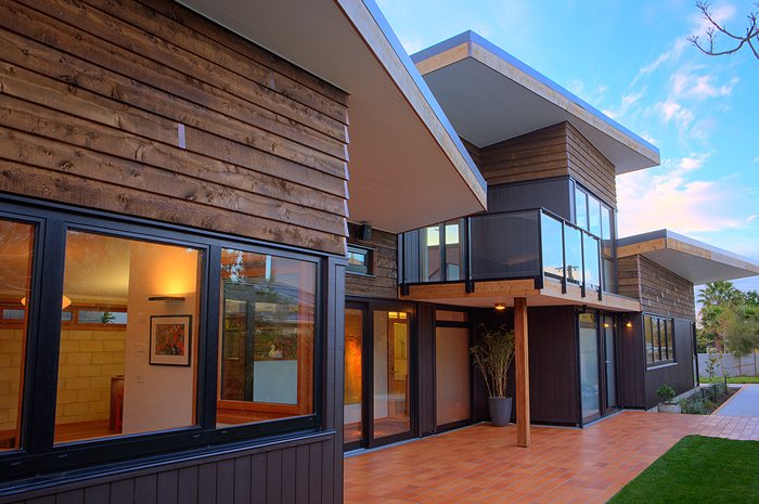 Home with vertical timber cladding, large windows and a balcony at dusk